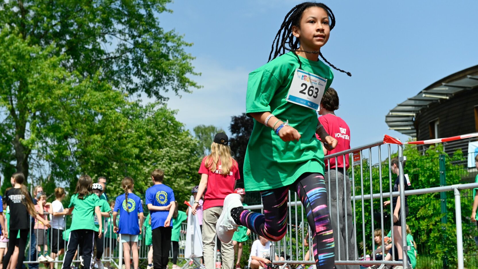 Ein Kind läuft mit Startnummer auf dem T-Shirt. Im Hintergrund sind weitere Kinder und Erwachsene, teils von hinten, zu sehen.