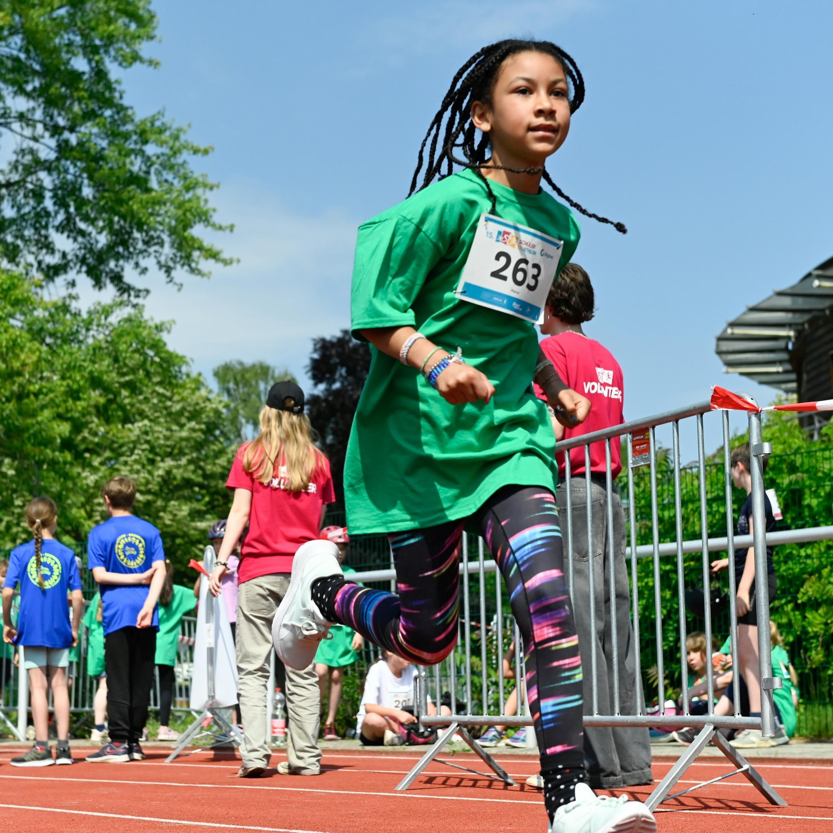 Ein Kind läuft mit Startnummer auf dem T-Shirt. Im Hintergrund sind weitere Kinder und Erwachsene, teils von hinten, zu sehen.