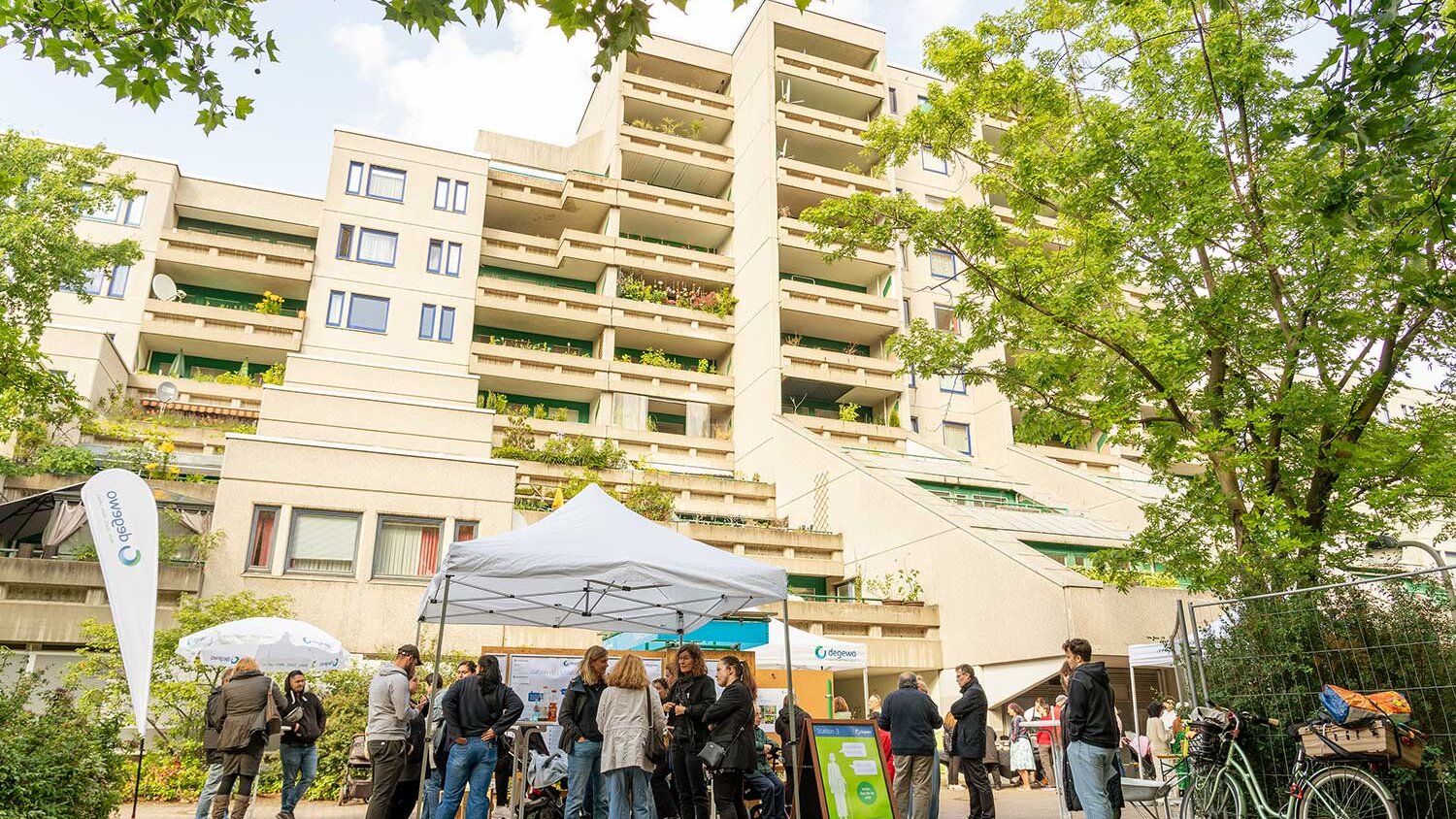 Menschen versammeln sich vor einem Wohngebäude unter einem Pavillon bei einer Informationsveranstaltung