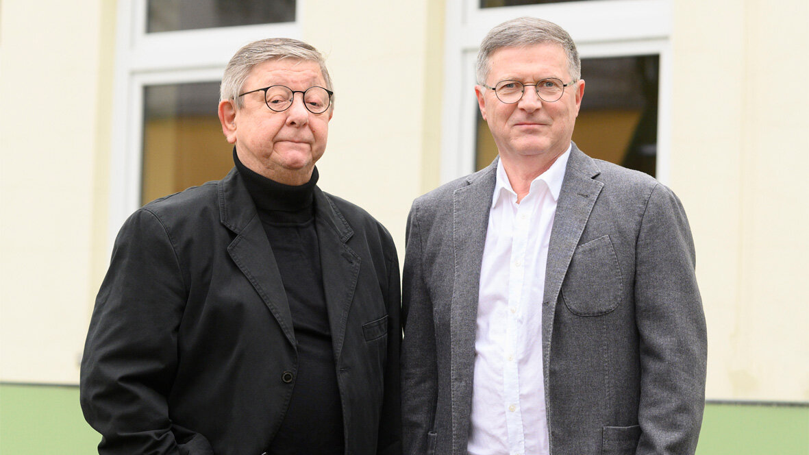Portrait des Mieterbeirates. Zwei Männer stehen im Freien vor einer Häuserwand mit Fenstern und schauen freundlich in die Kamera.