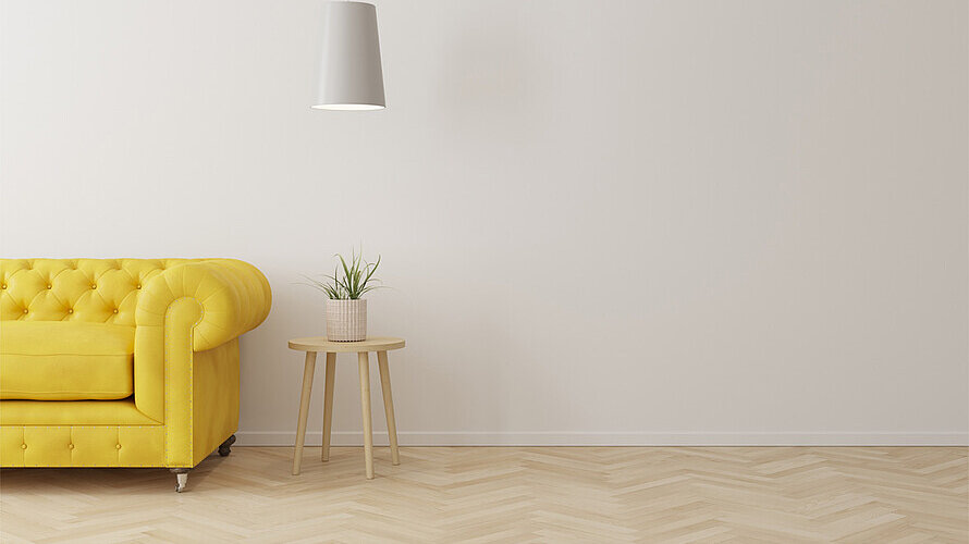 Ein leerer Raum mit gelbem Sofa und einem Hocker mit einer Pflanze.