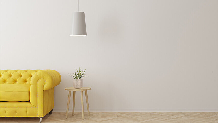 Ein leerer Raum mit gelbem Sofa und einem Hocker mit einer Pflanze.