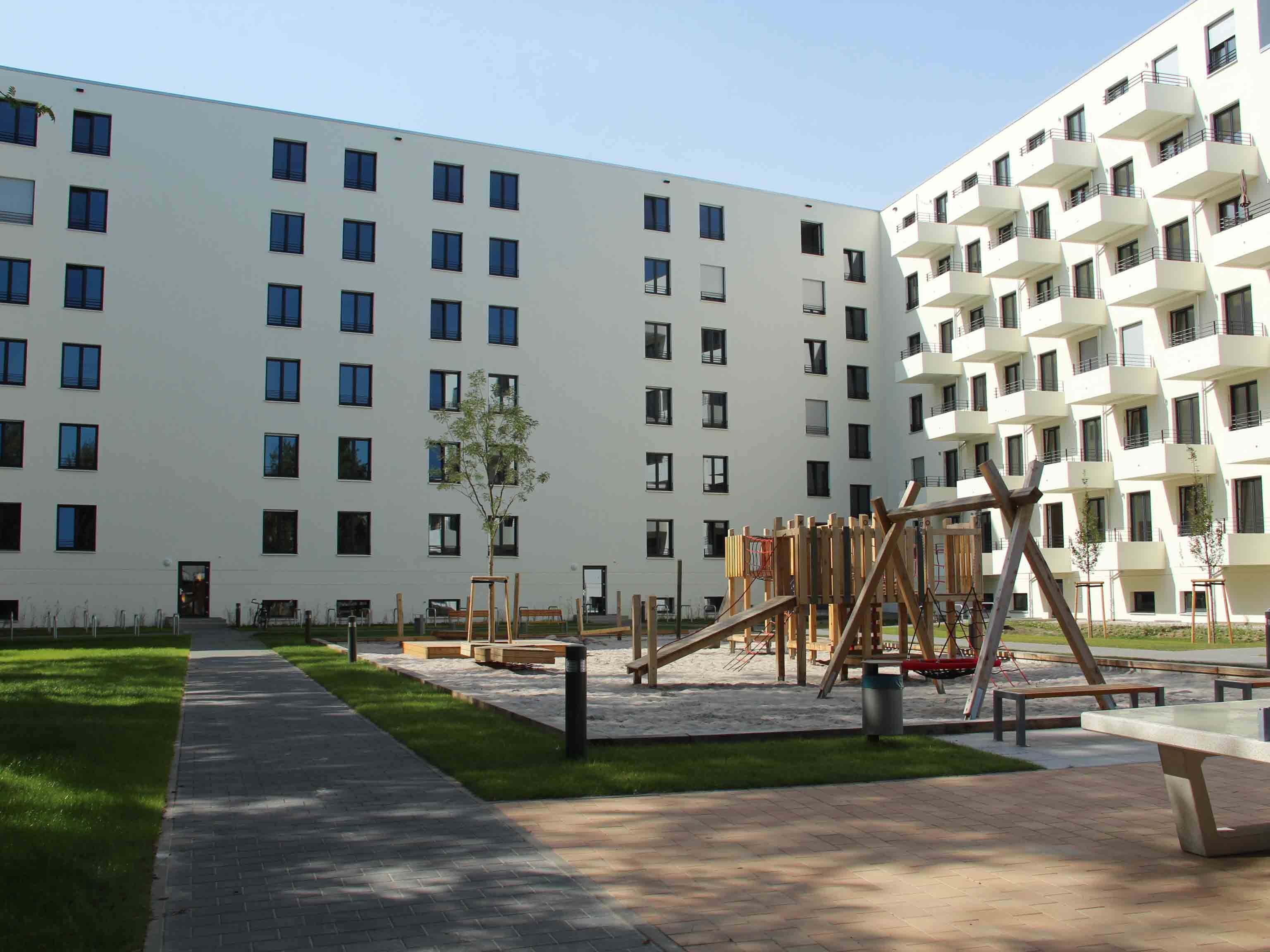 Außenansicht degewo-Neubau Graunstraße Gleimstraße: Hofseite mit Spielplatz sowie Weg, Rasenfläche und Tischtennisplatte im Vordergrund.