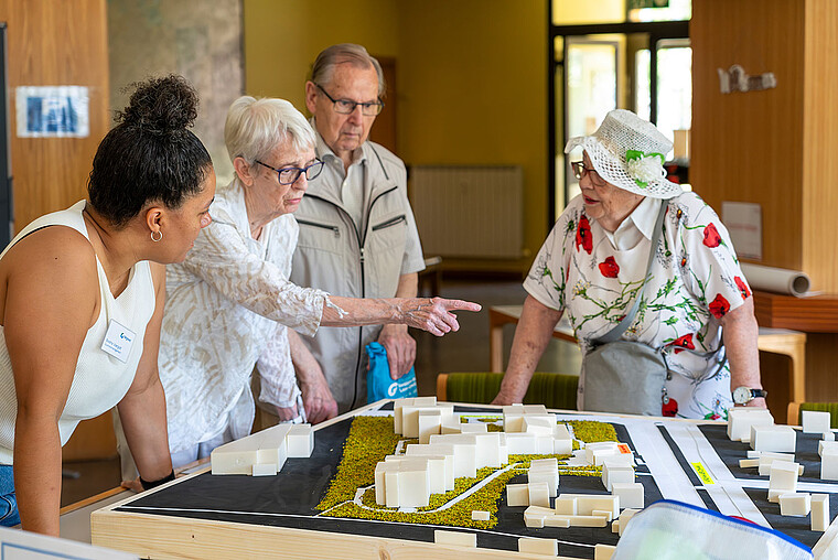 Vier Personen stehen um ein architektonische Modell einer Gebäudesanierung und informieren sich über den aktuellen Stand.