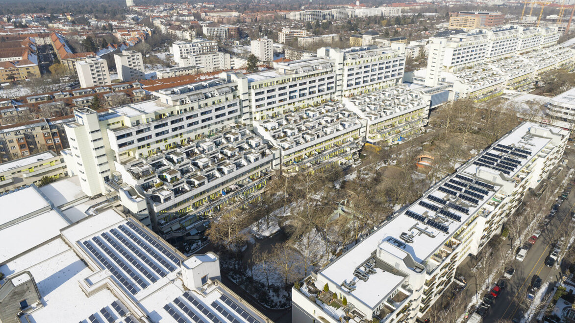 Luftaufnahme der Schlangenbader Straße in Berlin mit den markanten terrassenförmigen Wohngebäuden und verschneiten Dächern, umgeben von Stadtvierteln und Straßen.