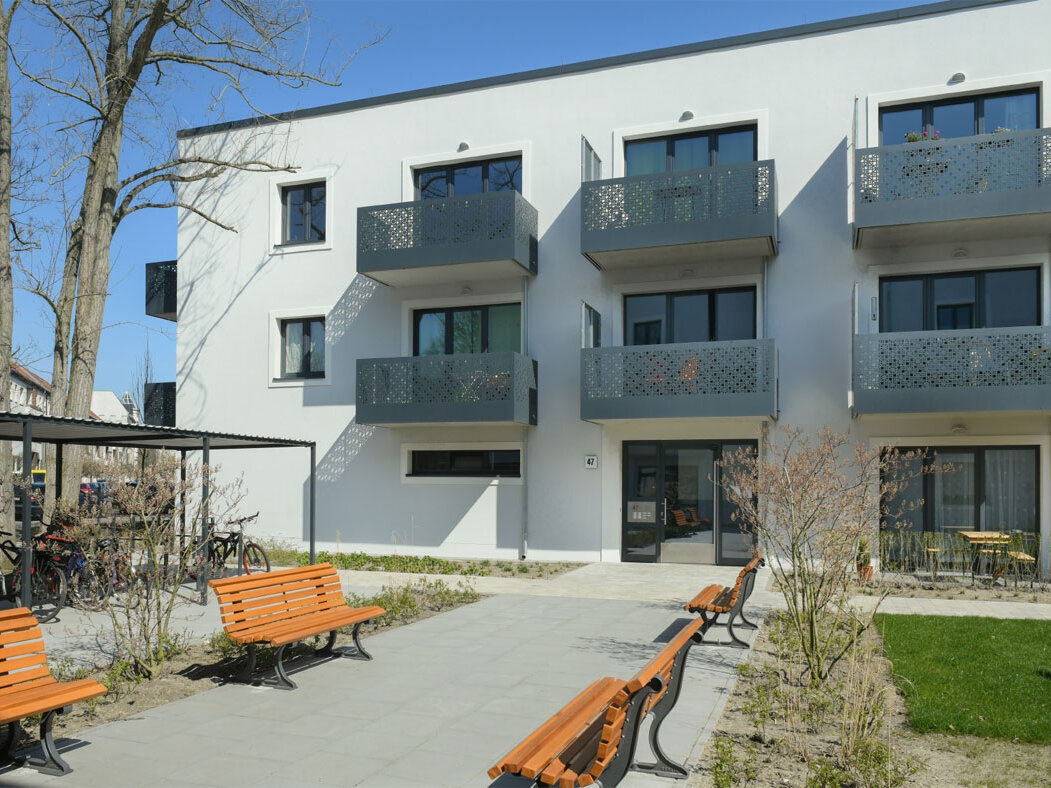 Außenansicht degewo-Neubau Rudower Straße 47 bis 51: Hofseite mit Weg, Sitzbänken und Grünfläche.