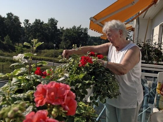 Eine Seniorin kümmert sich um rote Blumen auf dem Balkon