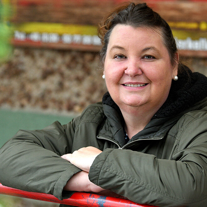 Eine Frau stützt sich auf ein Geländer und blickt freundlich in die Kamera.