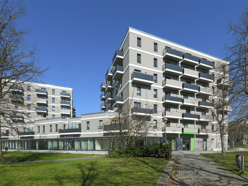 Außenansicht degewo-Neubau Mehrower Allee 28 und 30 mit Rasenflächen, Wegen und Bäumen im Vordergrund.