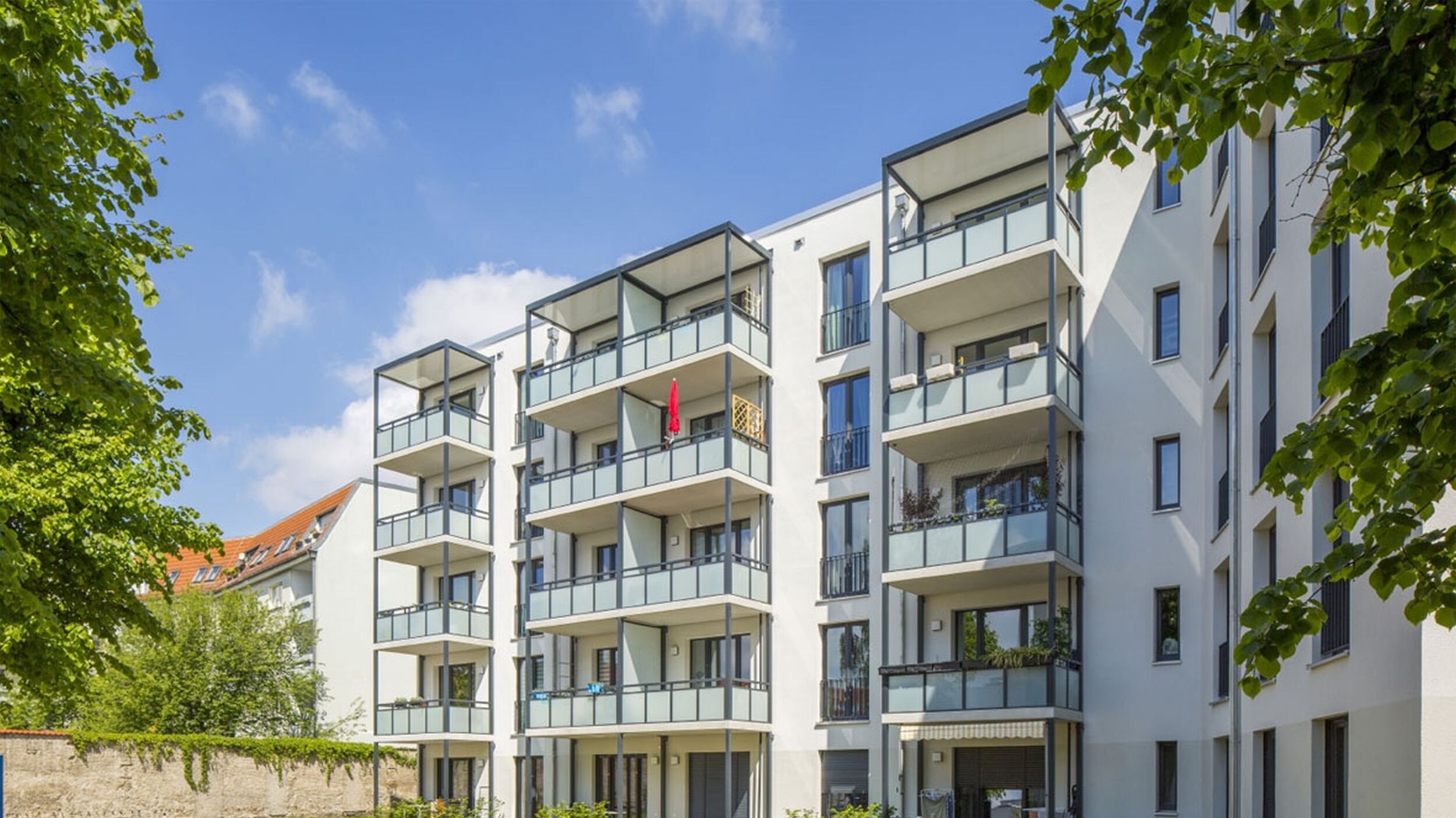 Außenansicht degewo-Neubau Luisenstraße 24 bis 24 A: Hofseite mit Grünfläche und beblätterten Zweigen links und rechts im Vordergrund.