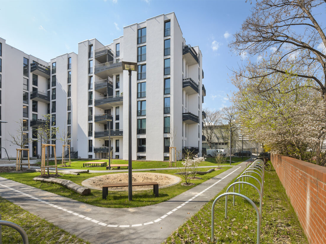 Außenansicht Hofseite degewo-Neubau Lützowstraße 7 mit Fahrradständern und Weg im Vordergrund sowie Mauer rechts.