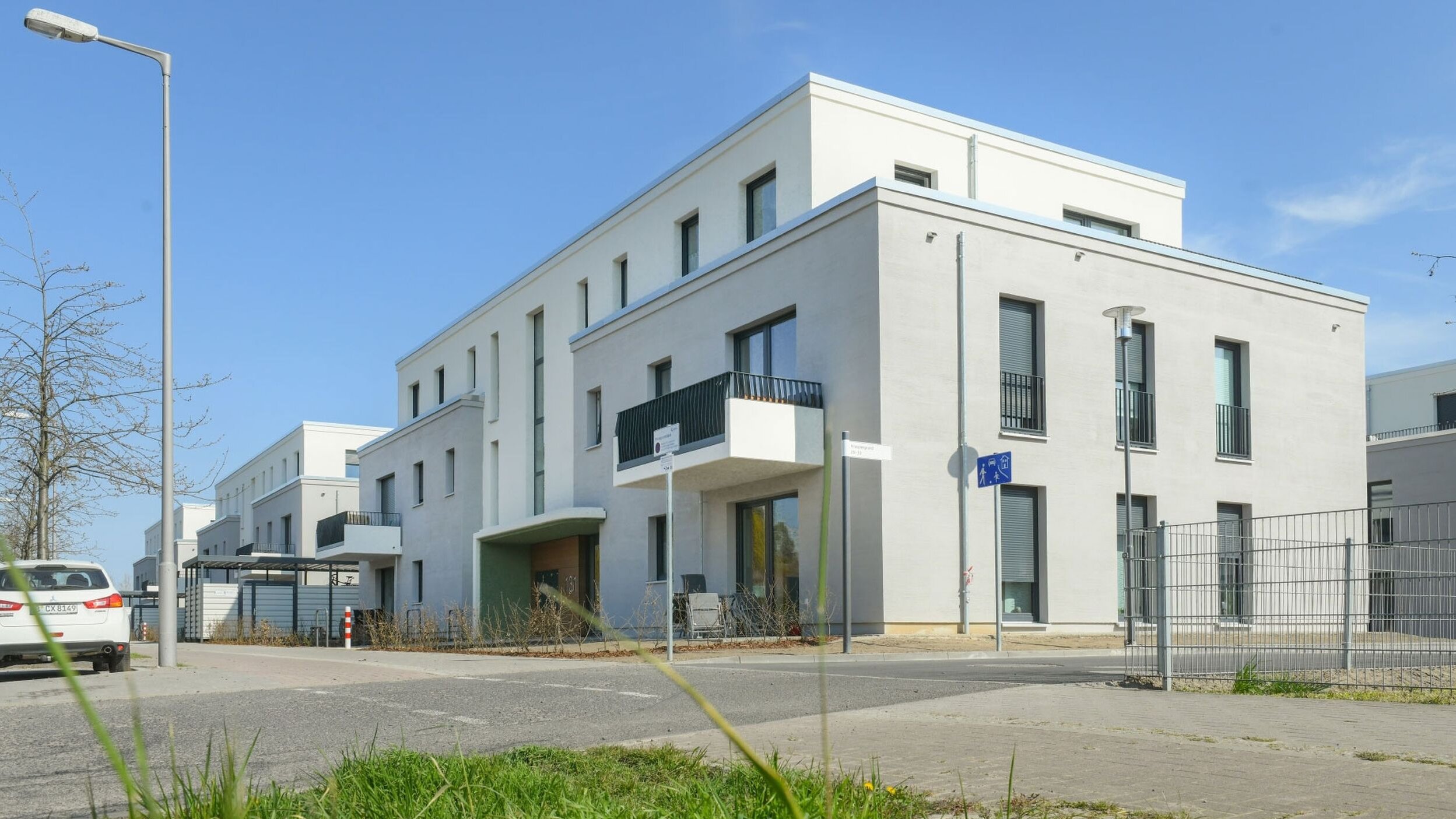 Außenansicht degewo-Neubau Bohnsdorfer Weg 127 bis 131 Knospengrund 27 bis 33 mit Grünfläche, Parkflächen und Straße im Vordergrund.