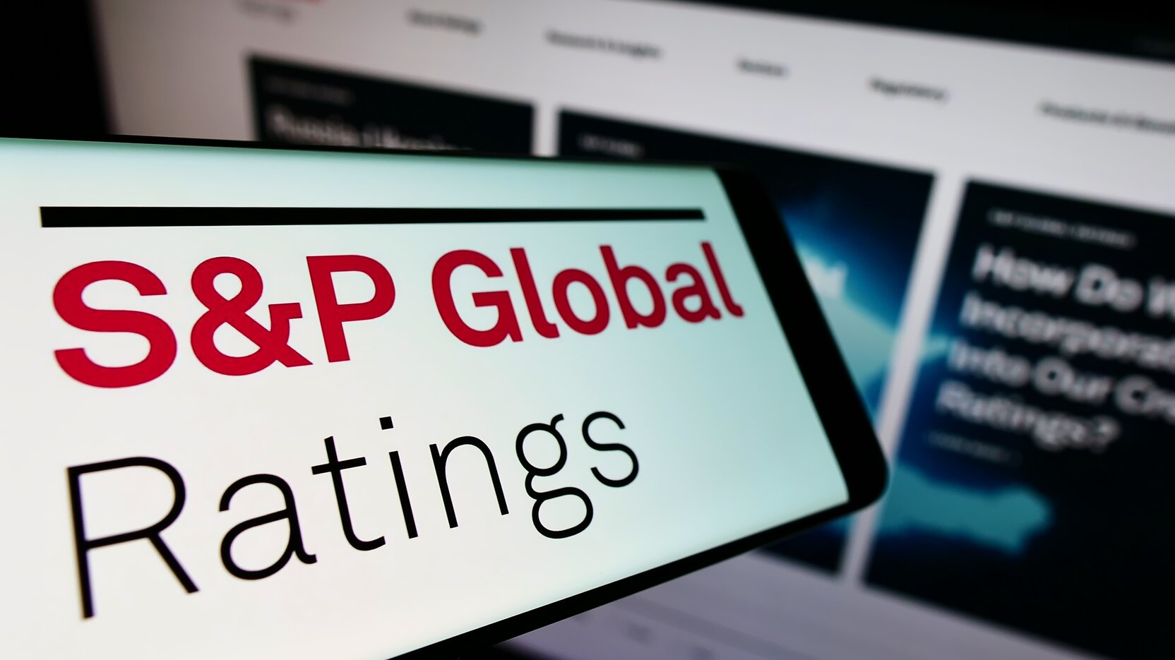 Vor einer verschwommenen Webseite ist links unten auf einem Bildschirm zu lesen: S&P Global Ratings.