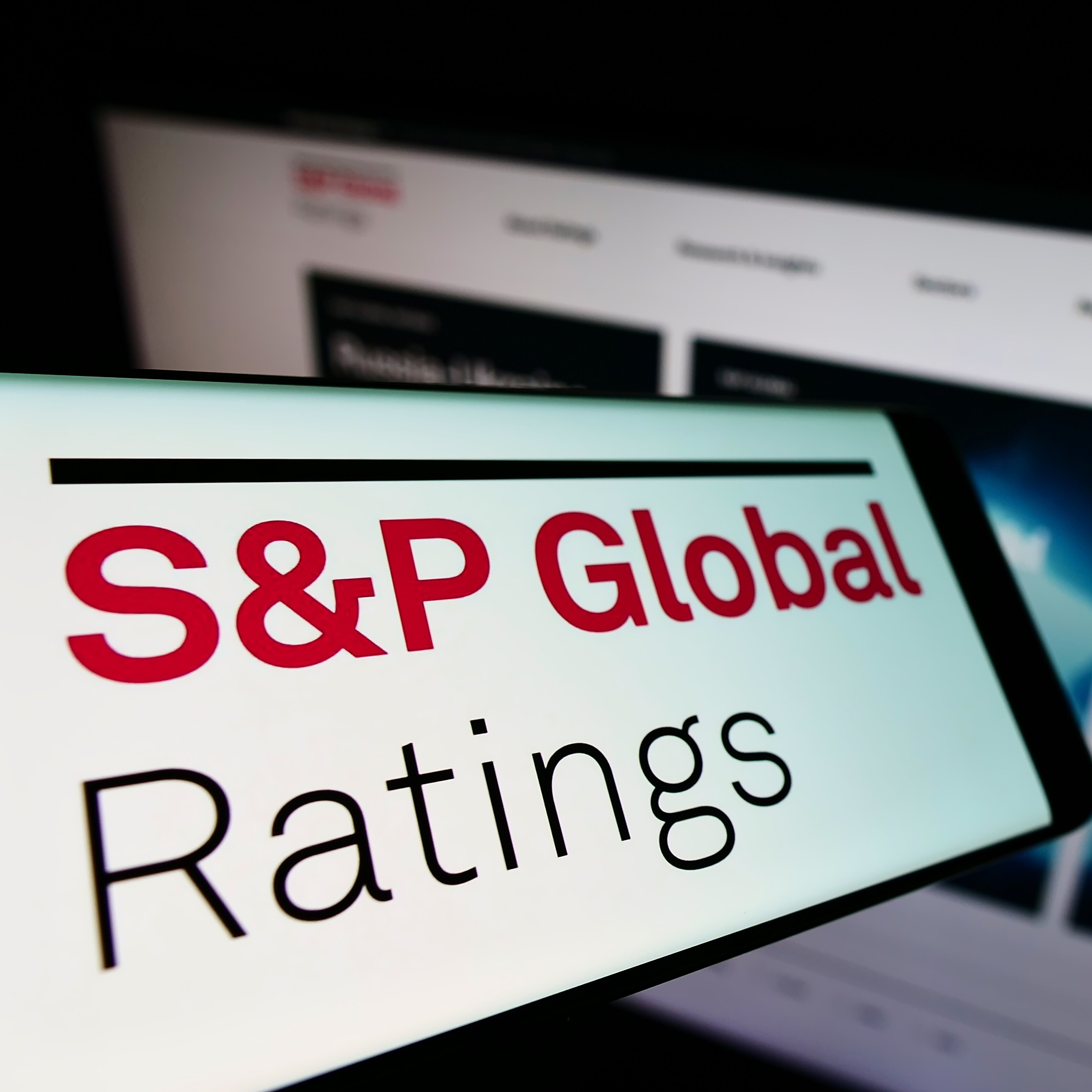 Vor einer verschwommenen Webseite ist links unten auf einem Bildschirm zu lesen: S&P Global Ratings.
