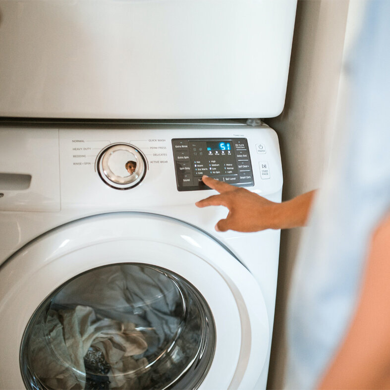 Person bedient das Bedienfeld einer laufenden Waschmaschine und stellt ein Programm ein.