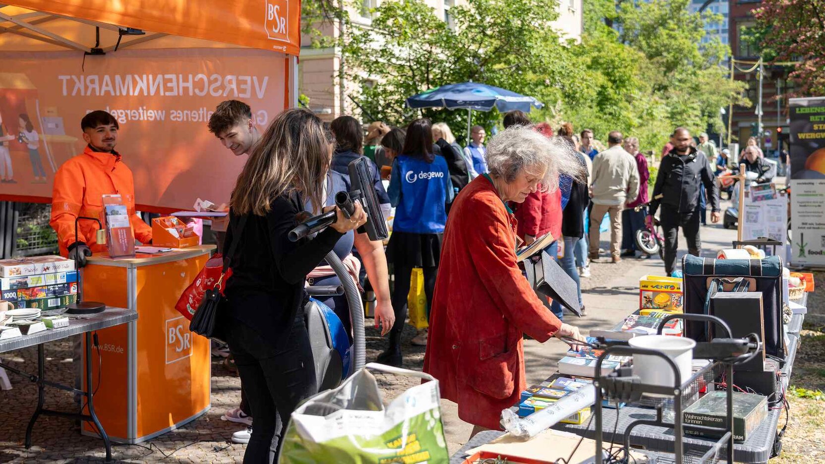 Menschen sind auf einer Straße und besuchen ein Kiezfest. Die schauen sich entlang der Stände um.