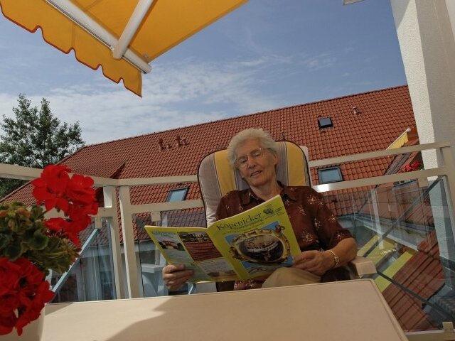 Eine Seniorin sitzt auf dem Balkon und liest Zeitung