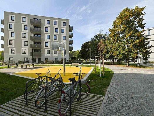 Außenansicht degewo-Neubau Max-Herrmann-Straße 14: Vorderseite mit Fahrradständern und geplasterter Straße im Vordergrund..