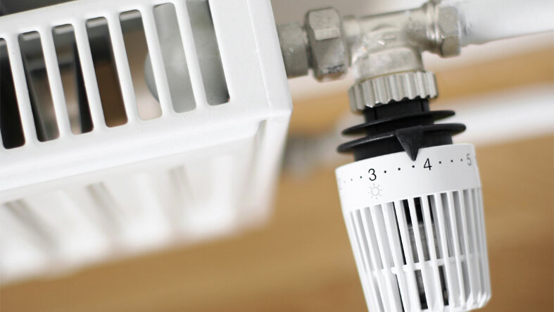 Nahaufnahme eines weißen Heizkörpers bei Tageslicht, das Thermostaat steht im Fokus.