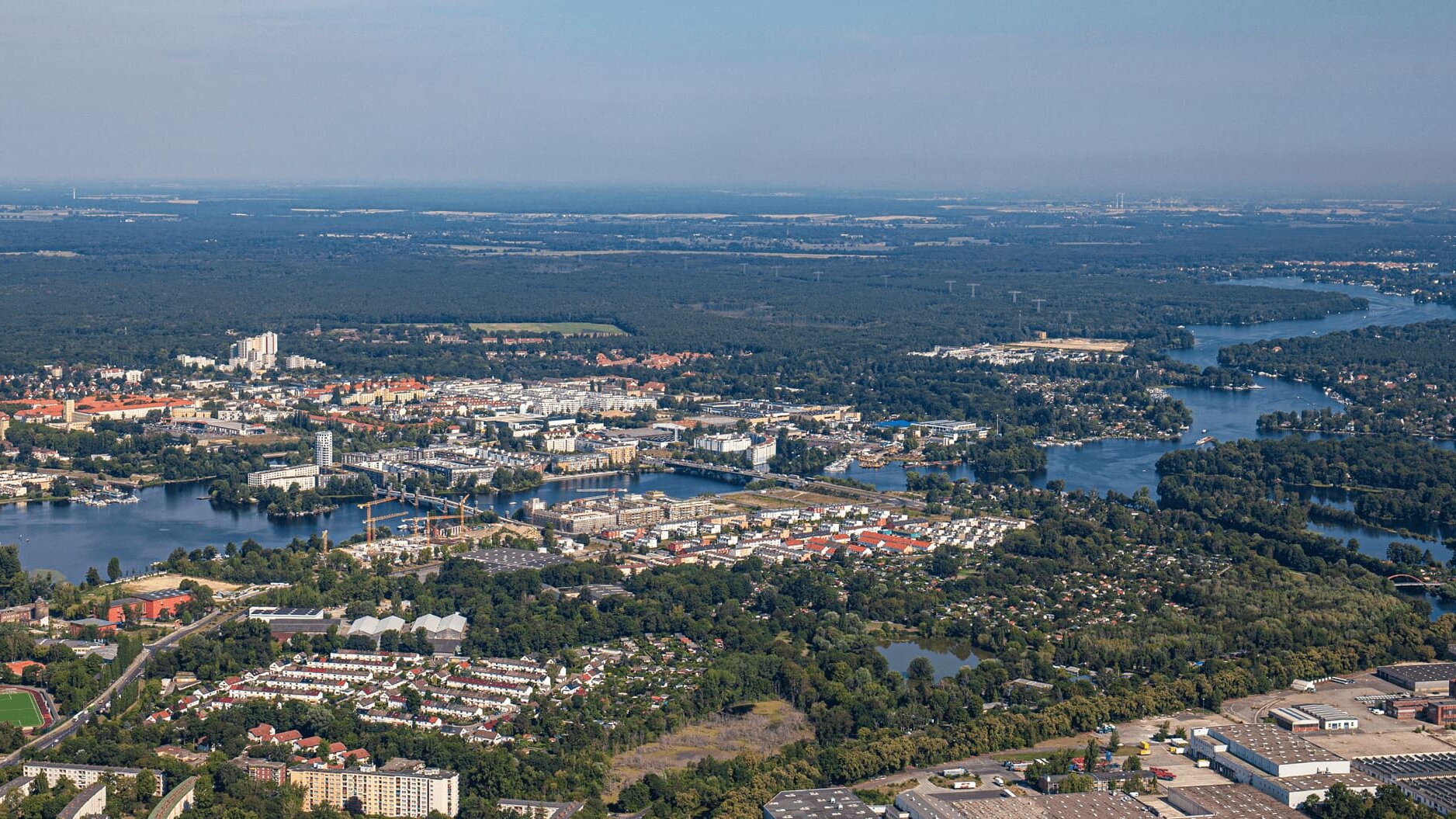 Ein Luftbild zeigt den Berliner Bezirk Spandau mit Wohngebieten, Flussläufen, Seen und großen Grünflächen aus der Vogelperspektive.