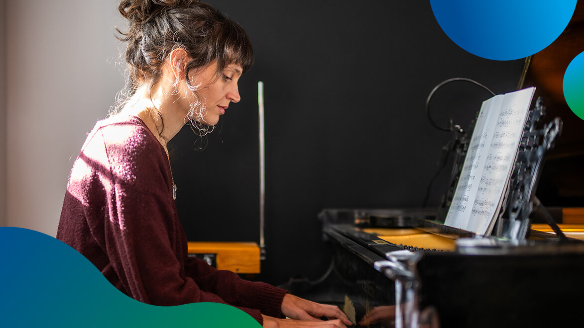 Eine Frau spielt an einem alten Klavier. Sonnenstrahlen scheinen von hinten auf sie. 