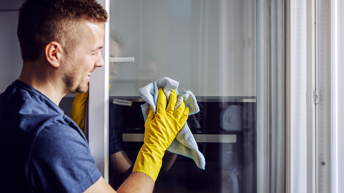 Ein Mann wischt ein Fensterglas mit einem Lappen.