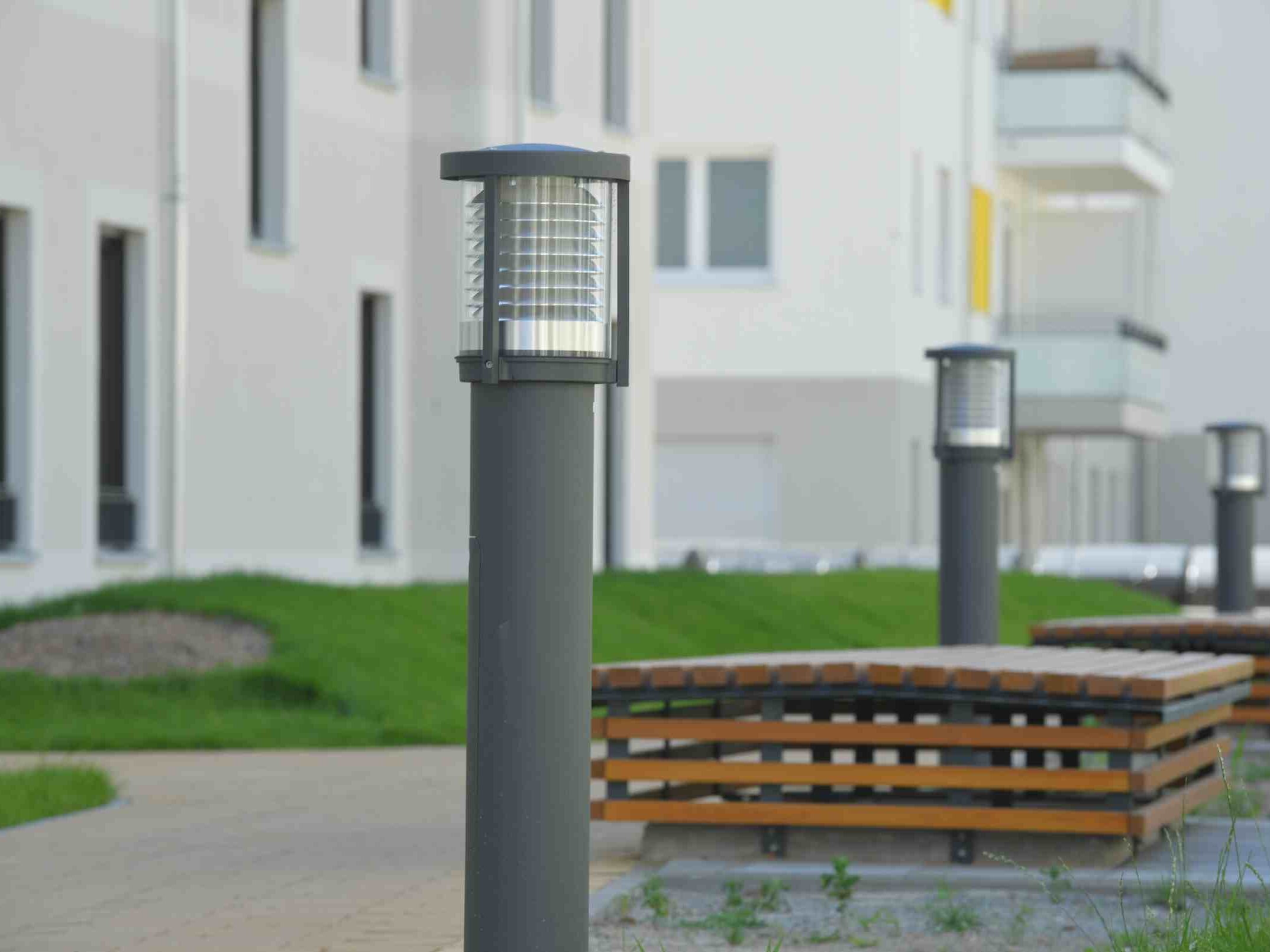 Außenansicht degewo-Ankauf Pepitahöfe: Hofseite mit gepflastertem Weg und Sitzgelegenheiten, Weglaterne im Vordergrund.