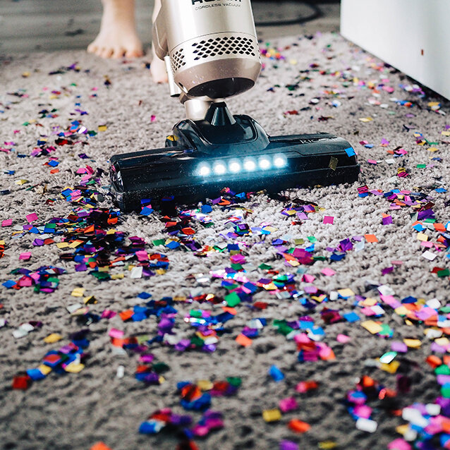 Der Staubsauger saugt kleine Fetzen farbigen Papiers auf einem flauschigen braunen Teppich auf.
