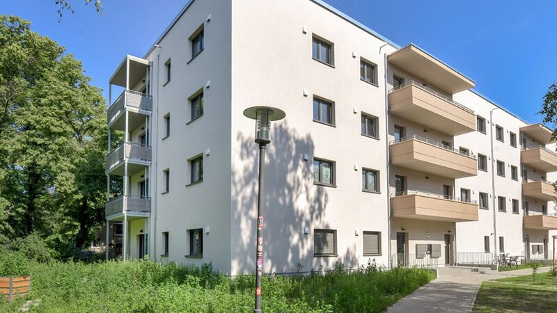 Außenansicht degewo-Neubau Ottomar-Geschke-Straße mit Grünflächen, Wegen und Straßenlaternen im Vordergrund.