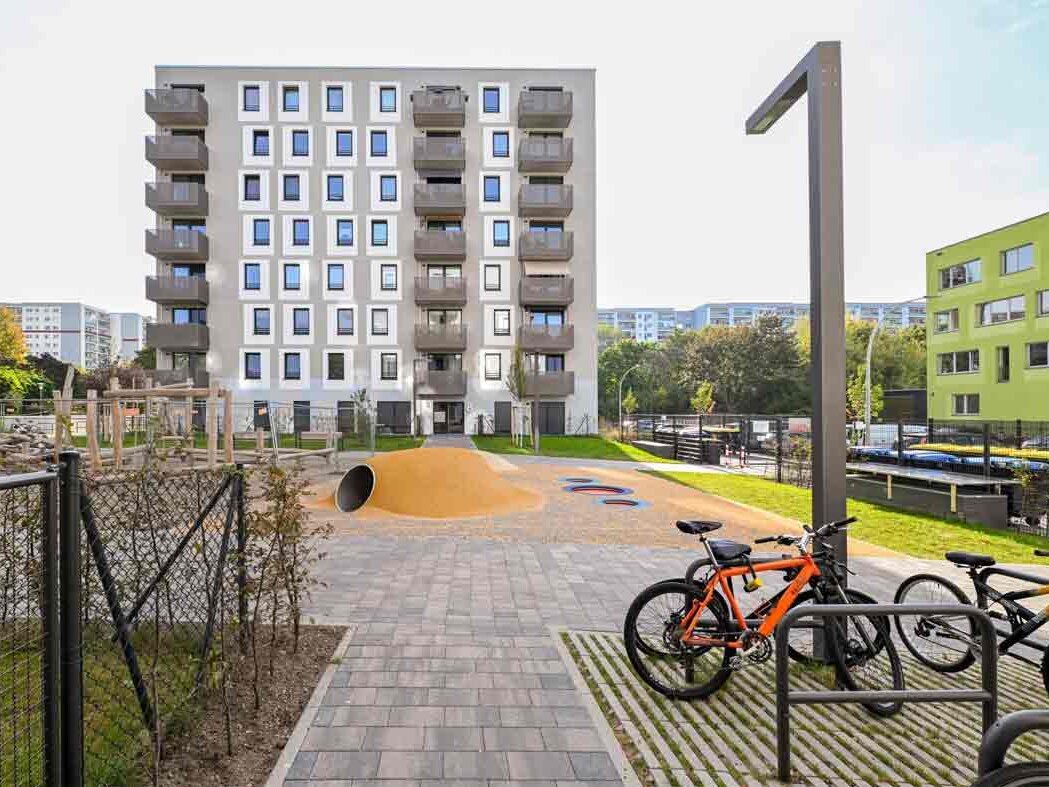 Außenansicht degewo-Neubau Max-Herrmann-Straße 8: Vorderseite mit Spielplatz und Fahrradständern im Vordergrund.