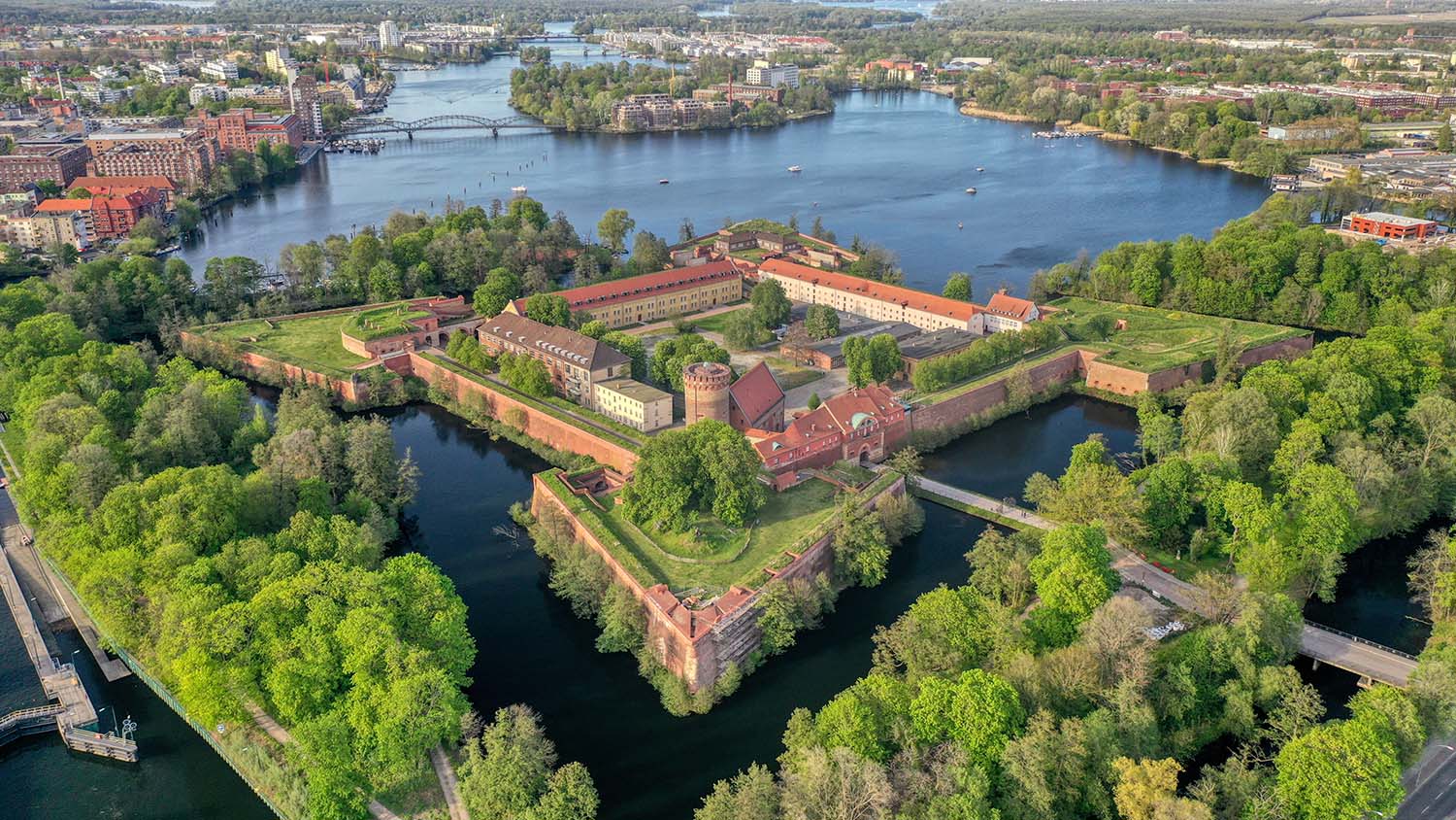 Luftaufnahme der Zitadelle Spandau, umgeben von Wassergräben, Bäumen und Gewässern.
