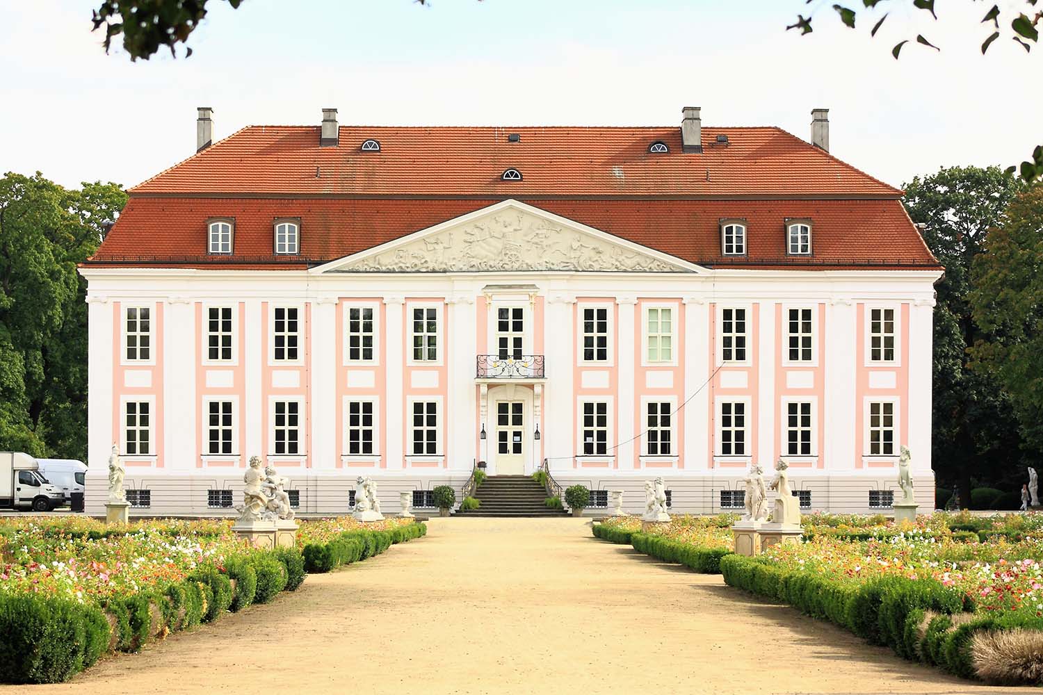 Historisches Schloss mit heller Fassade, rotem Dach und symmetrisch angelegtem Gartenweg.