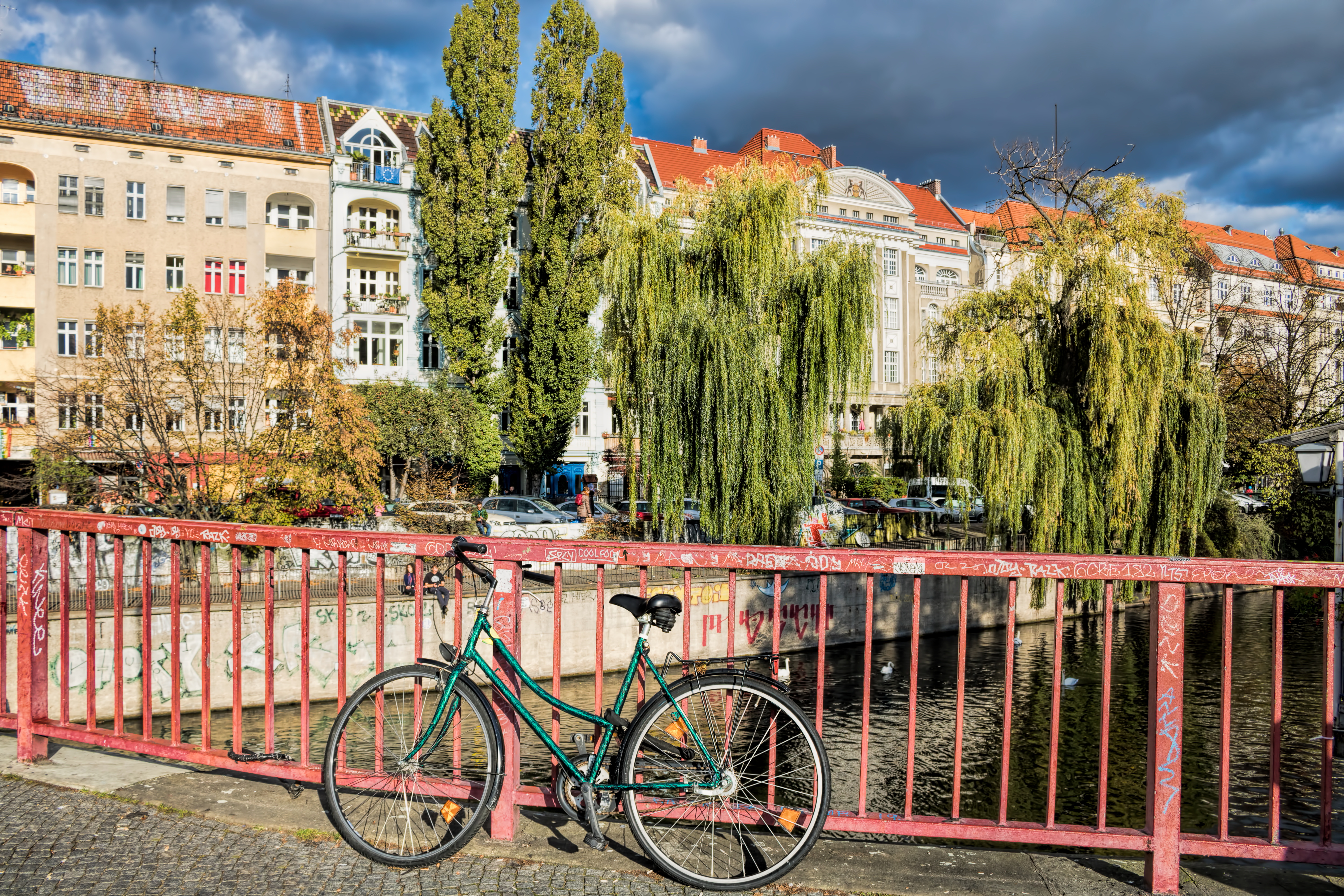 Fahrrad an einer Brücke über den Landwehrkanal mit Altbauten und Bäumen in Berlin-Neukölln.
