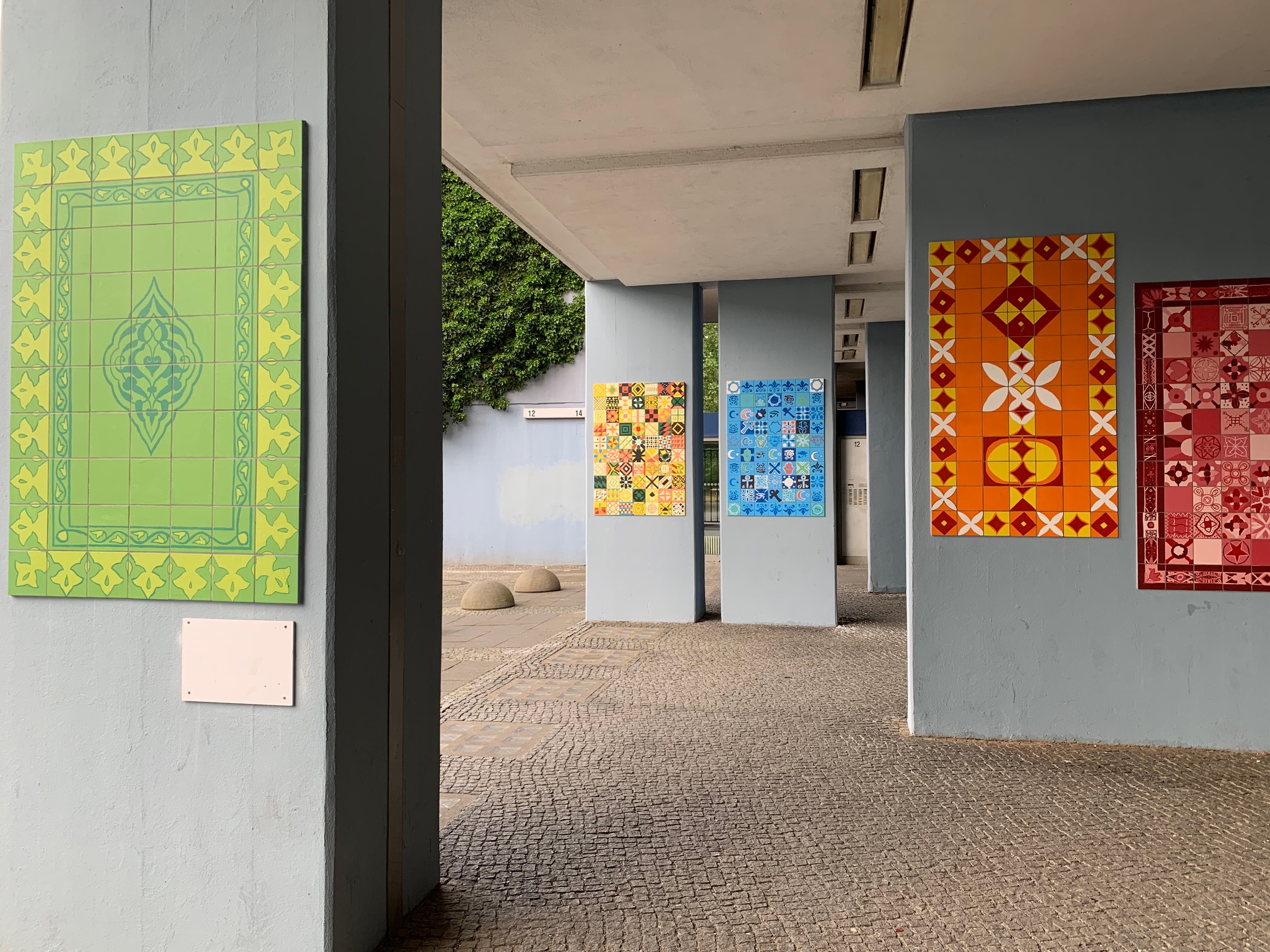Mehrere bunte Fliesenbilder auf hellgrauen Säulen.
