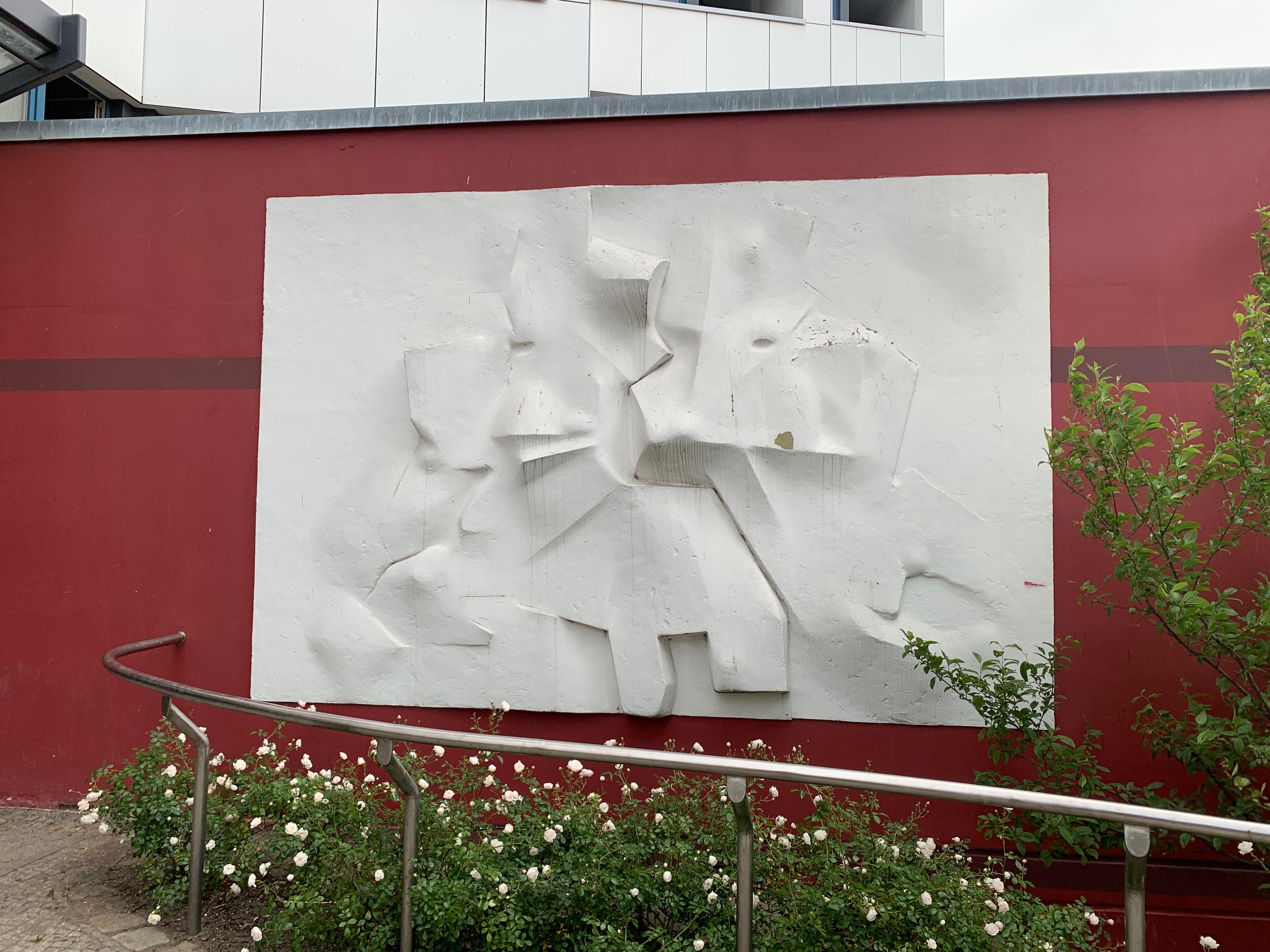 Ein weißes, dreidimensionales, abstraktes Wandrelief auf dunkelrotem Untergrund.