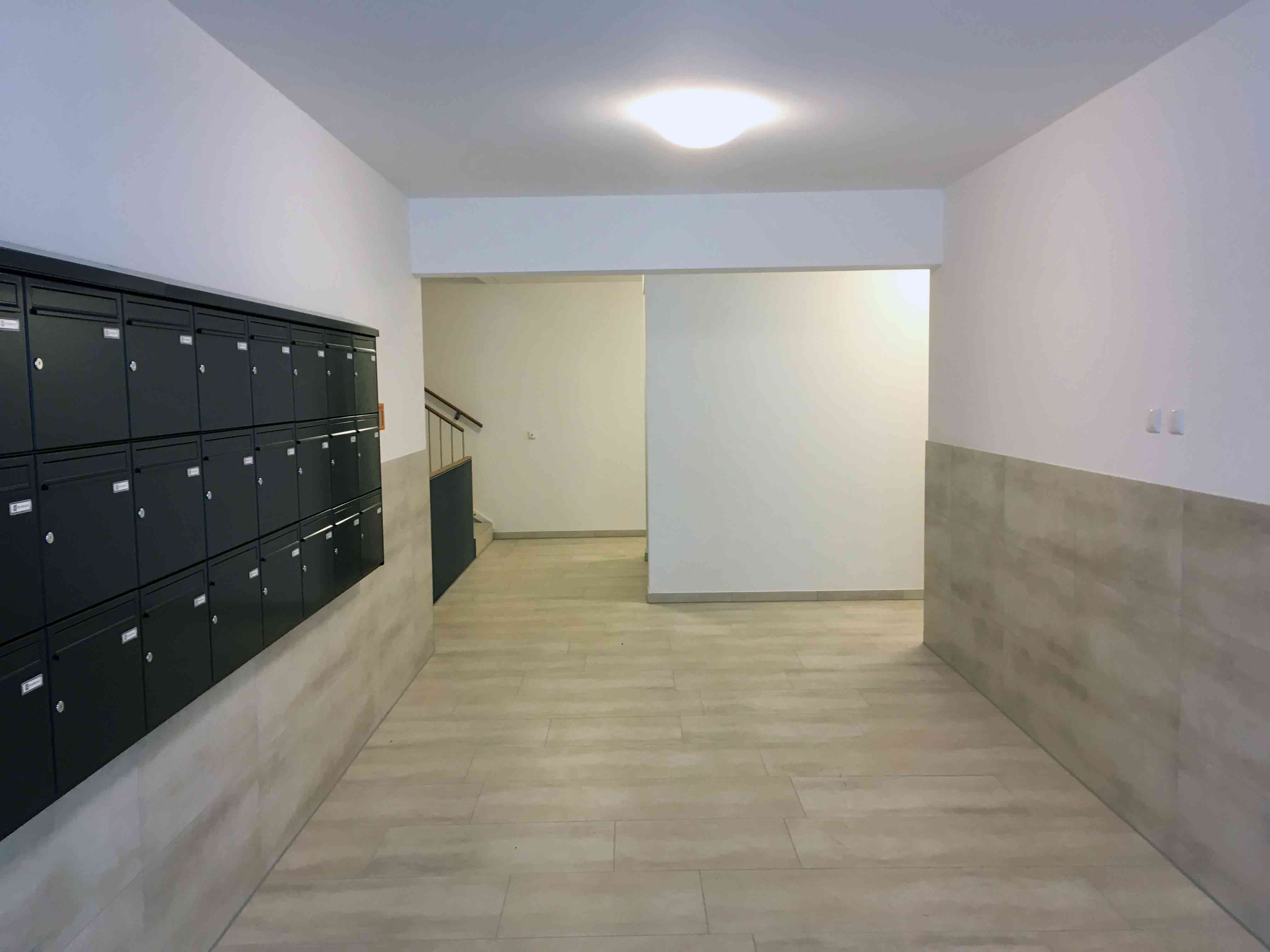 Innenansicht degewo-Neubau Abram-Joffe-Straße: beleuchteter Eingangsbereich mit Briefkästen links.