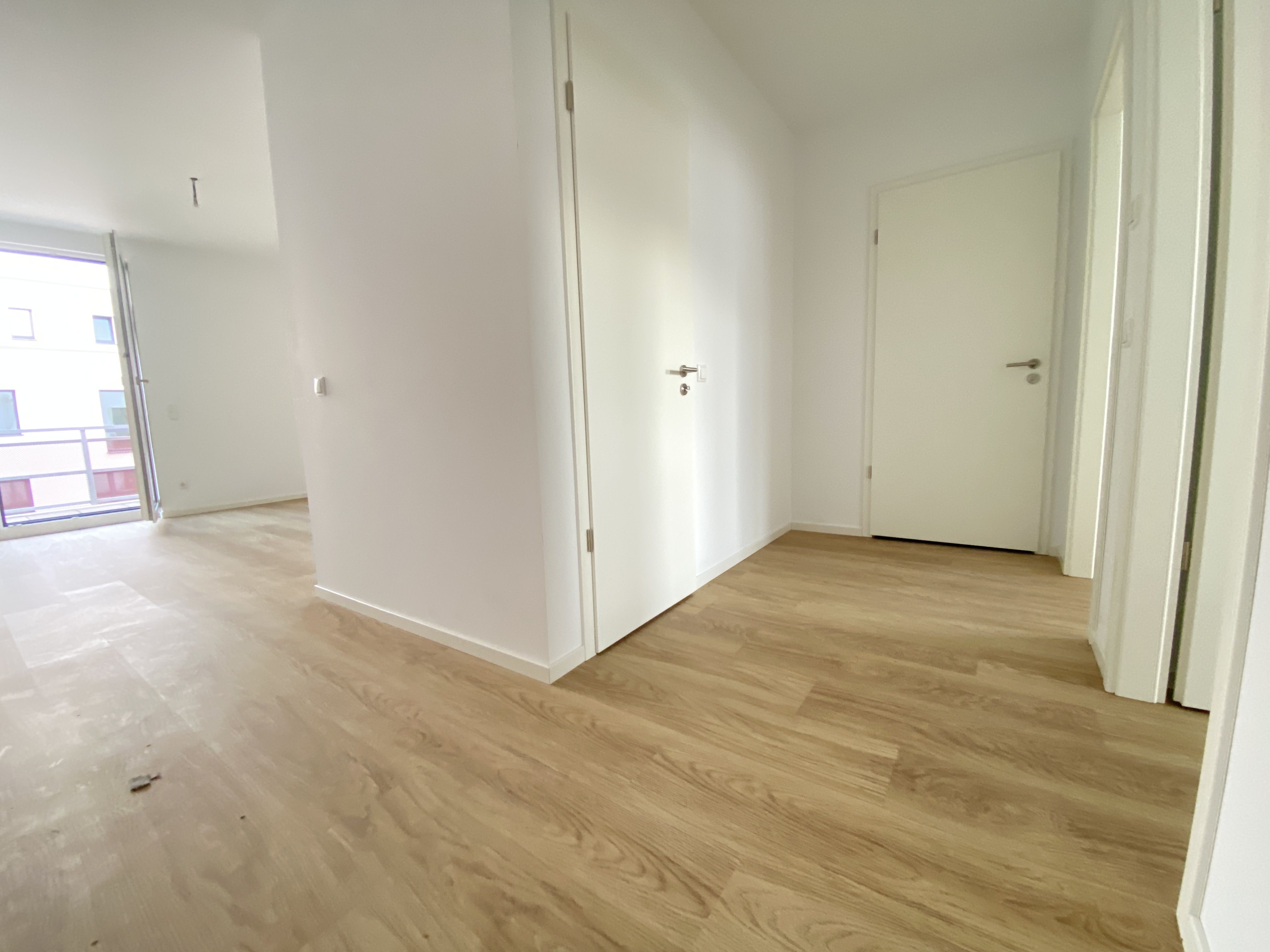 Innenansicht degewo-Neubau Fürstenwalder Allee 324/326: leeres Zimmer mit geöffneter Balkontür und Blick auf weitere Zimmertüren.