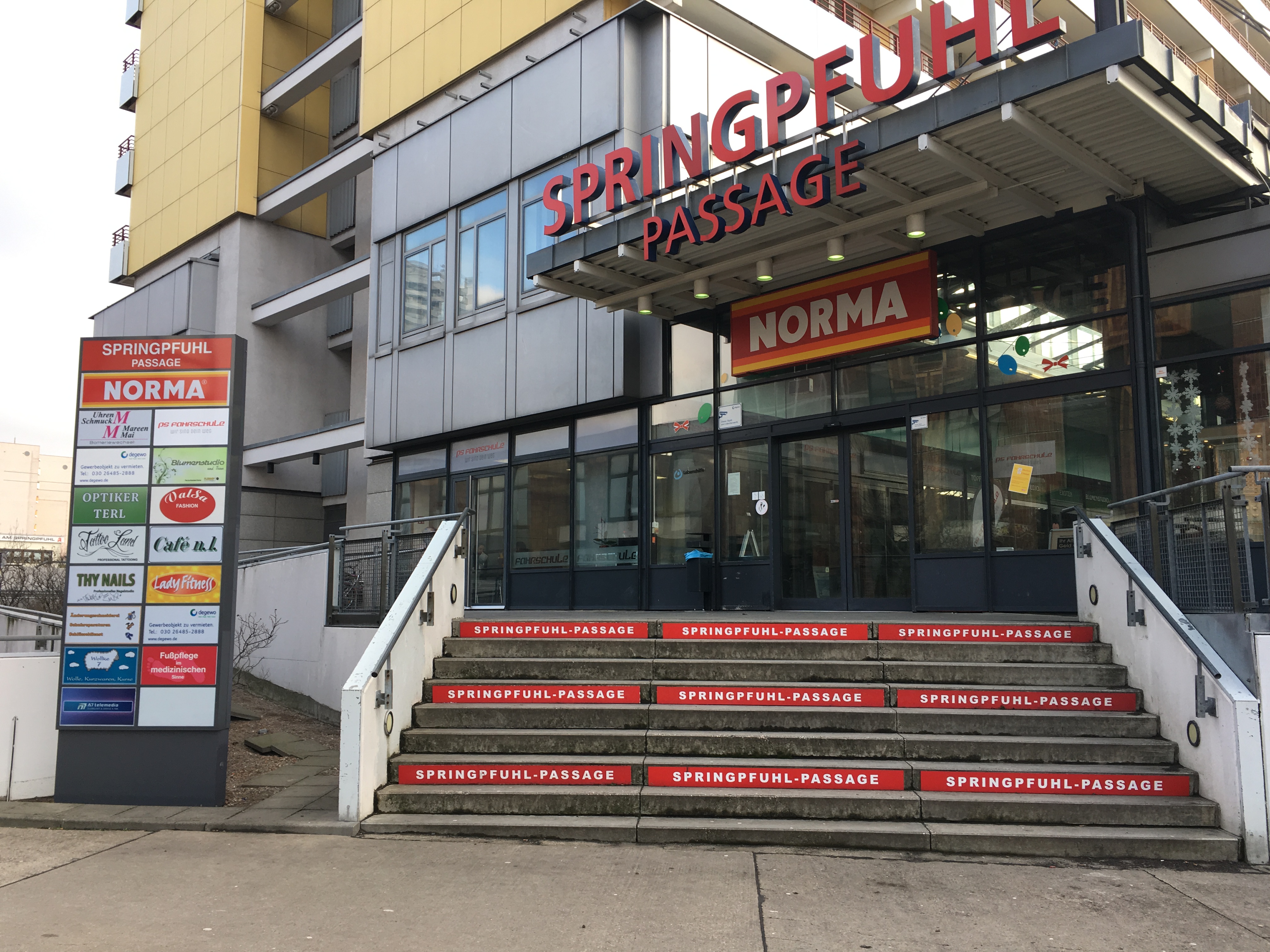 Blick auf eine breite Treppe mit Werbung zu einem Einkaufscenter unten im Hochhaus