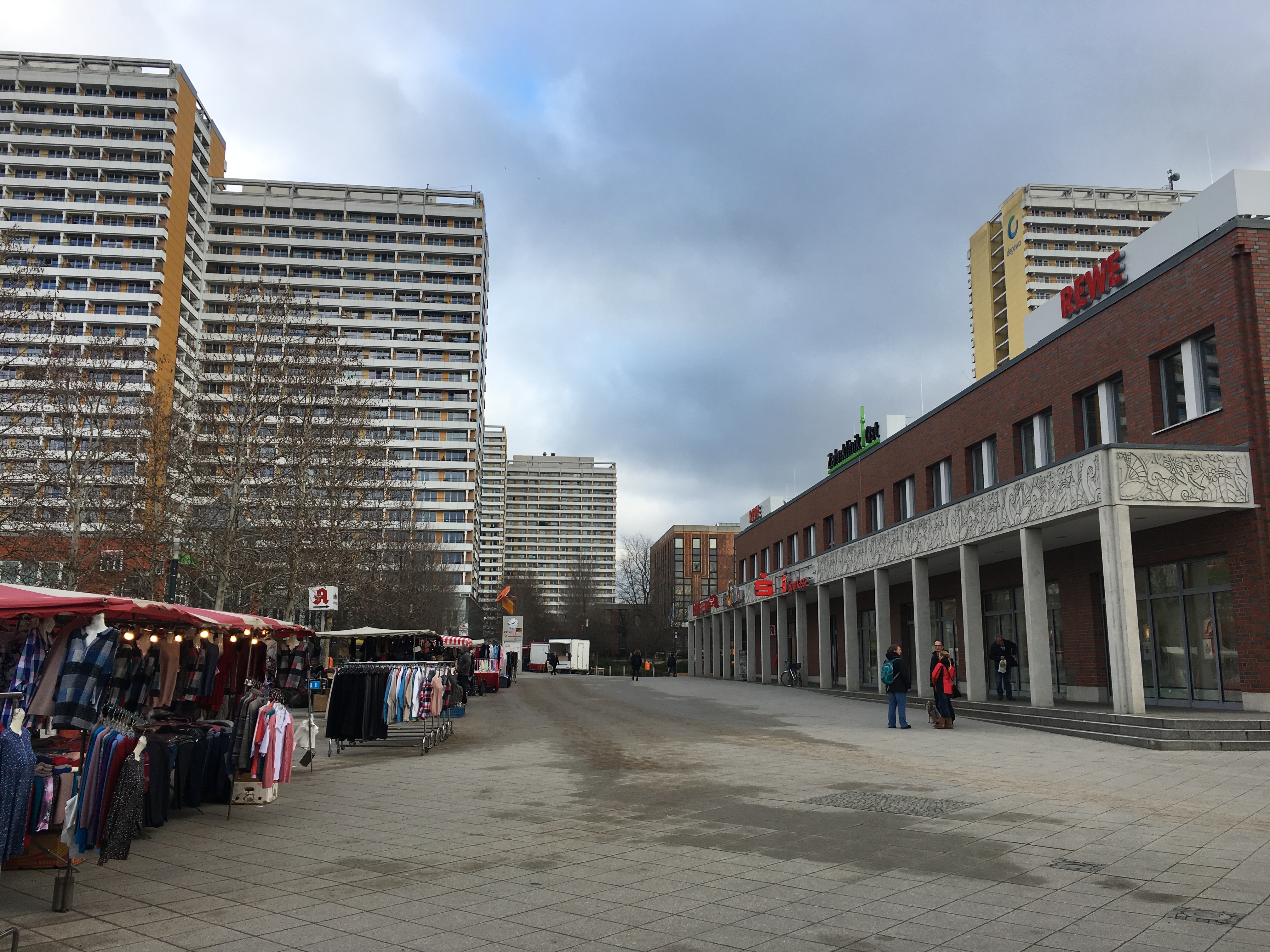 Ein Betonplatz, links Stände mit Kleidern, rechts ein Einkaufszentrum, im Hintergrund Hochhäuser