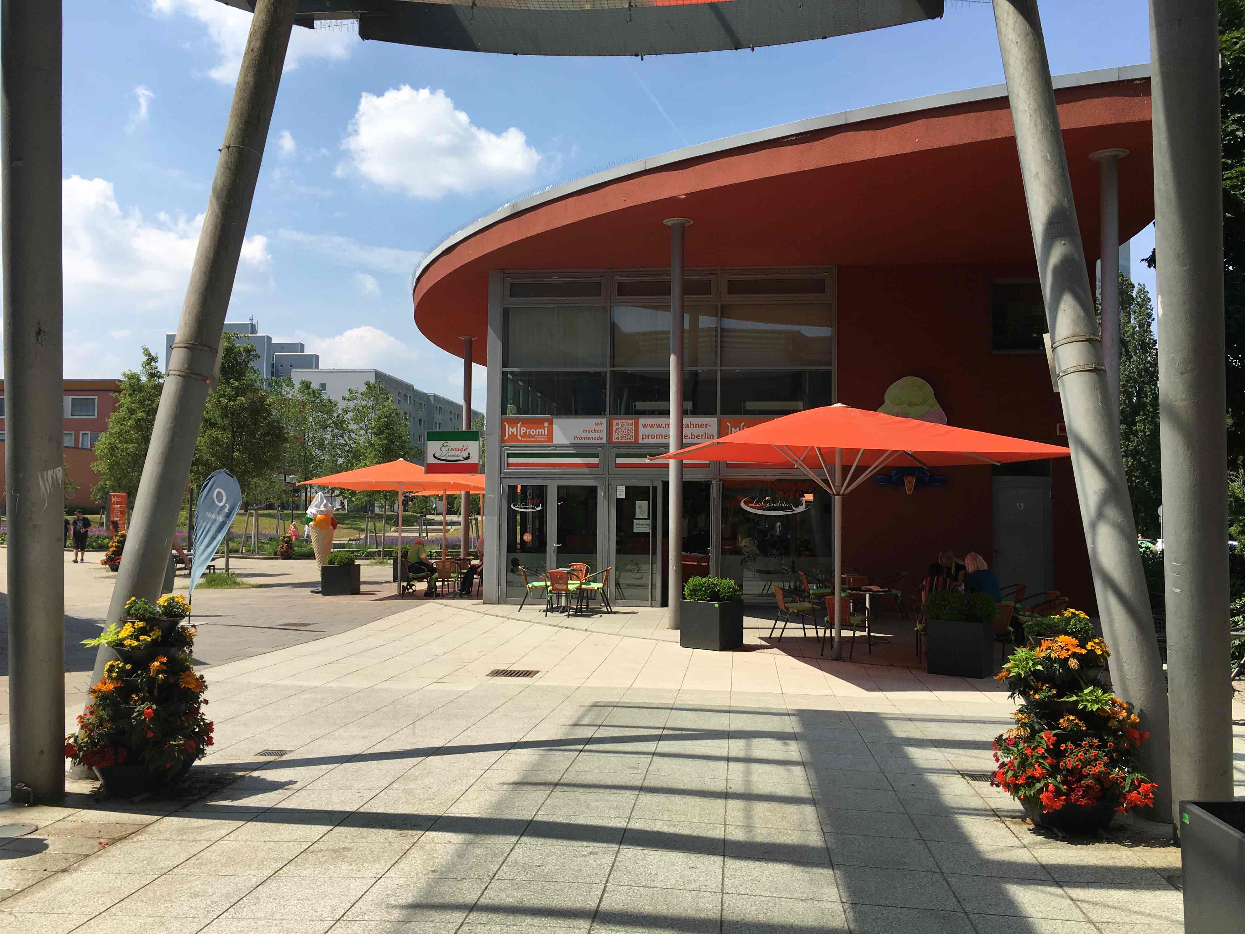 Betonierter Platz mit Blick auf Geschäfte in grauem Gebäude mit rotem runden Dach.