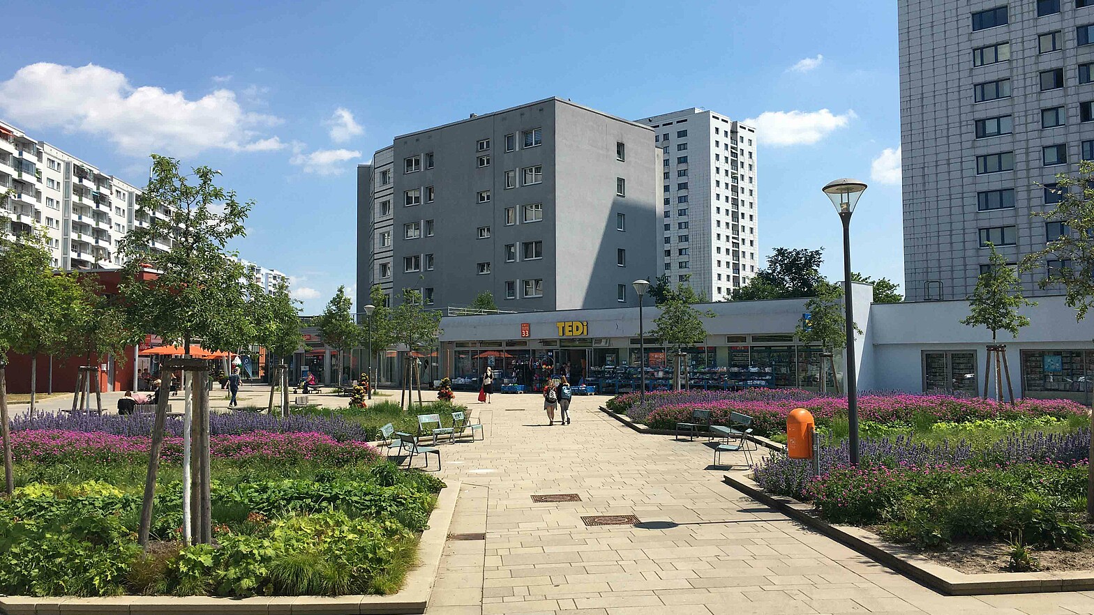 Blick auf die Promenade, ein Weg mit Grünabschnitten, Bänken und Laternen zwischen Hochhäusern